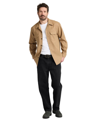 Man wearing a beige shirt, white t-shirt, black pants, and dark shoes on a white background