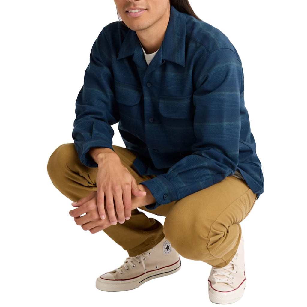 Man wearing a blue shirt and beige pants sitting on a white background