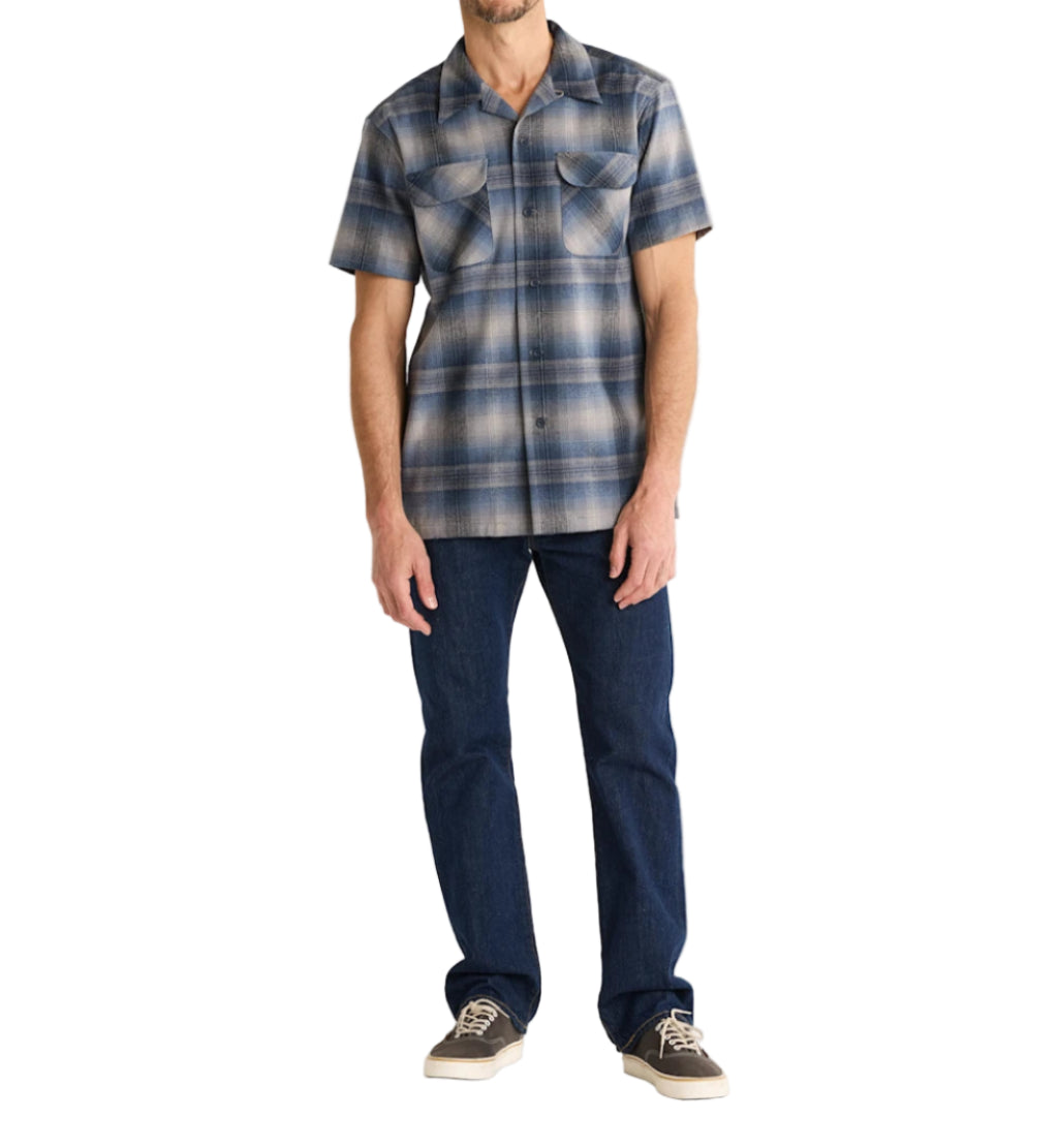 Man wearing a plaid short-sleeve shirt and dark jeans on a white background