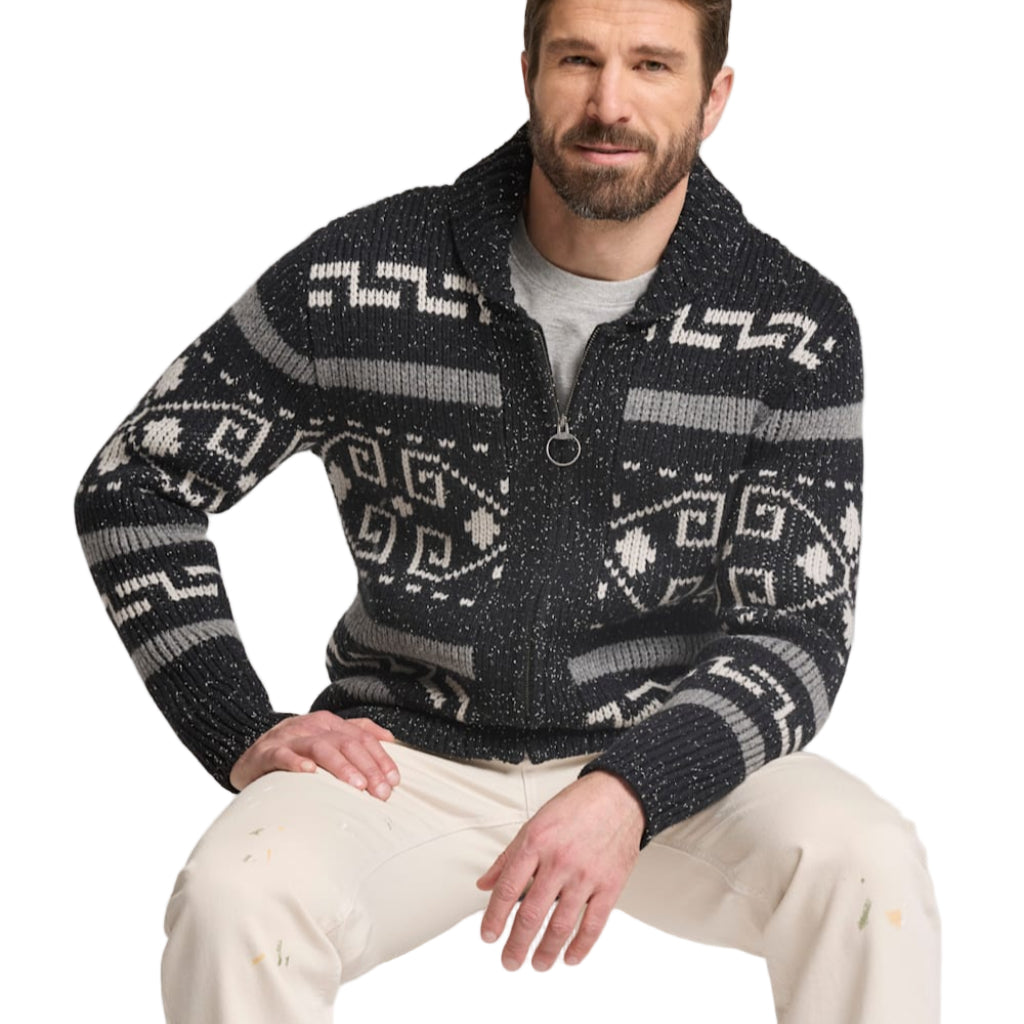 Man wearing a patterned sweater sitting against a plain background