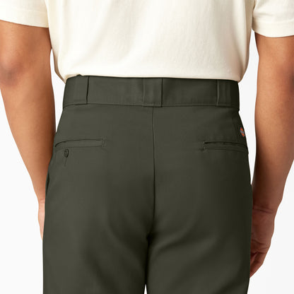 Person wearing dark green pants and a white shirt on a plain background
