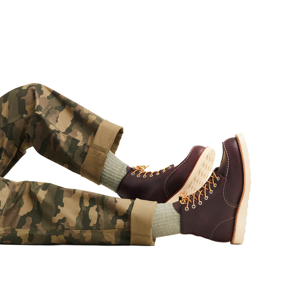 Brown leather boots with gold laces worn with camouflage pants on a white background