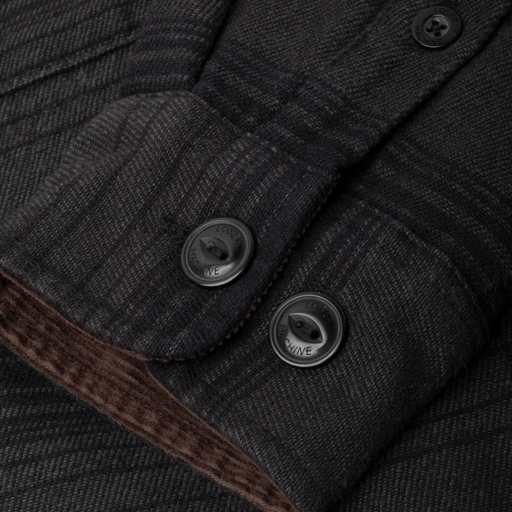 Close-up of a dark gray textured fabric with buttons and brown trim.