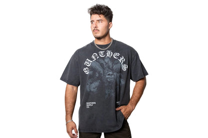 A man wearing a faded black Gunthers graphic t-shirt with a large gothic logo and posed against a plain white studio background.