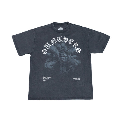 A dark charcoal gray short-sleeve t-shirt with a distressed graphic print. The design features the word 'GUNTHERS' in a stylized white gothic font arched over a detailed illustration 