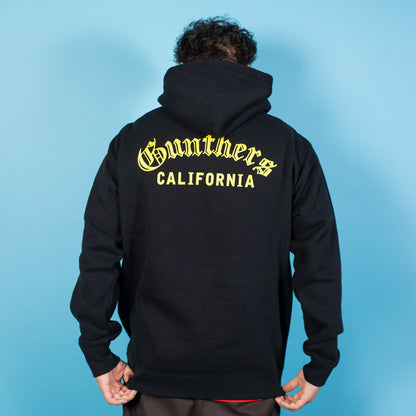Person wearing a black hoodie with 'Gunthers California' text on the back against a blue background