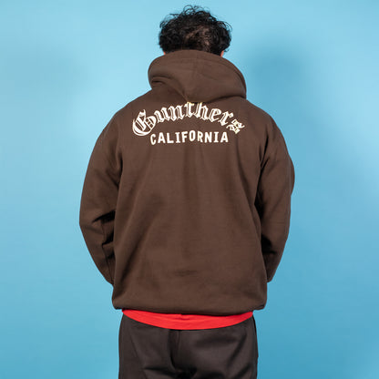 Person wearing a brown hoodie with 'Gunther's California' text on the back against a blue background