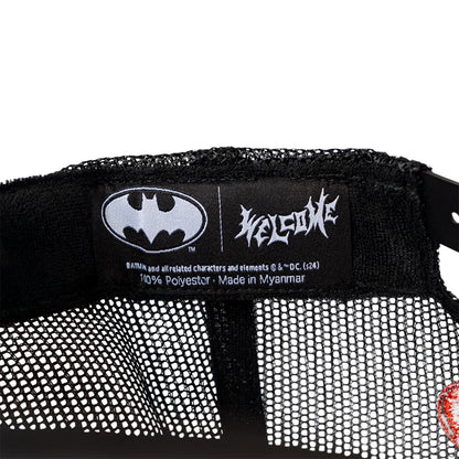 Close-up of a Batman logo on a label with 'Welcome' branding, on a black and white textured background.