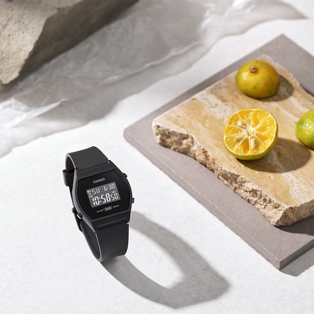 Black Casio digital watch on a light surface with a stone slab and lemons in the background