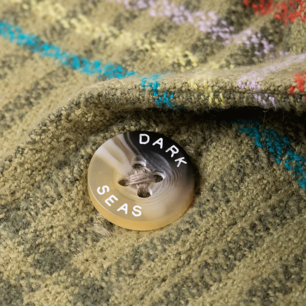 Close-up of a button with 'Dark Seas' branding on a textured fabric background