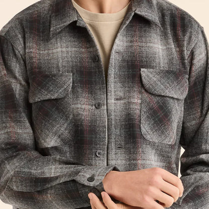 A person wearing a long-sleeved, square-bottomed, plaid shirt with two bias-cut pockets.