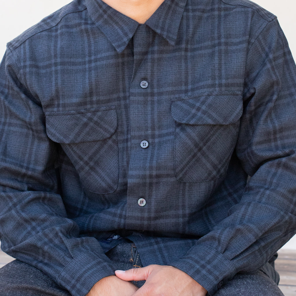 Person wearing a blue plaid shirt sitting on a wooden floor.