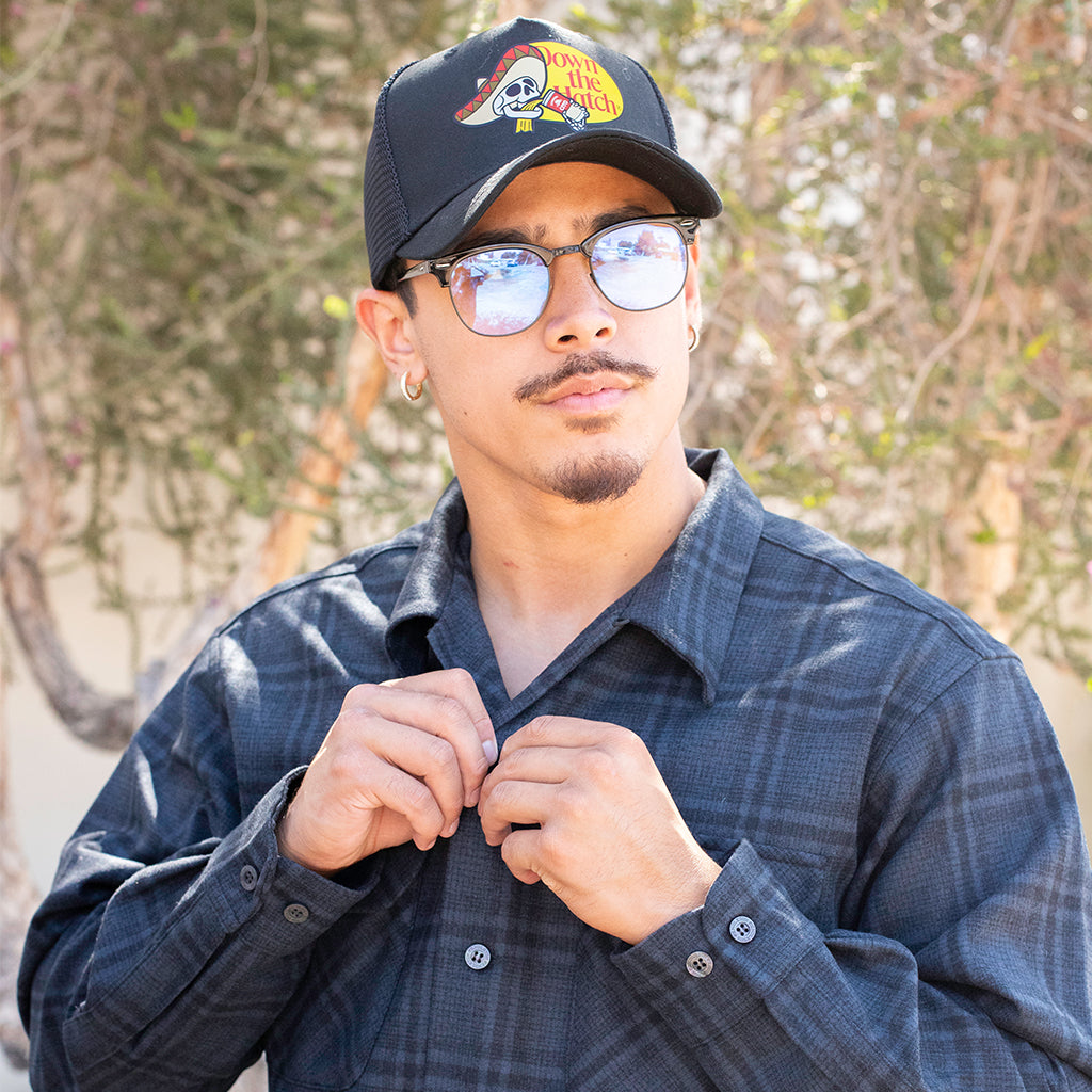 Man wearing a cap and glasses with a dark blue pendleton blurred natural background
