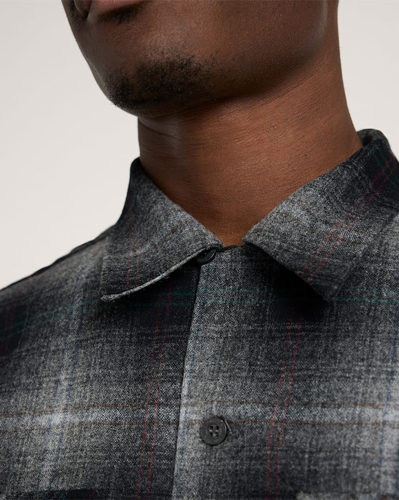 Close-up of a person wearing a gray checkered shirt with a neutral background