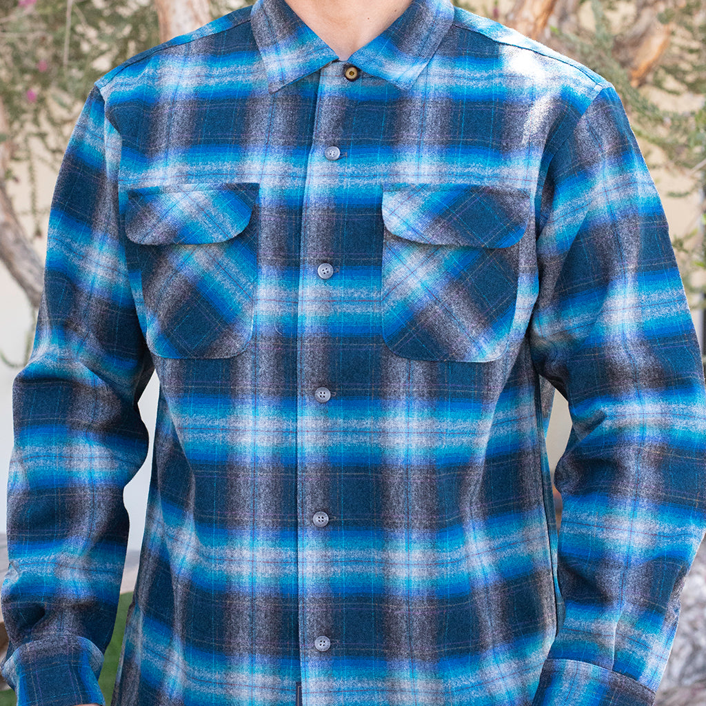 Blue and gray plaid shirt worn by a person with a blurred natural background