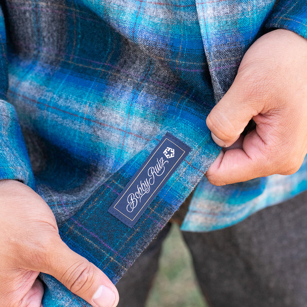 Close-up of a blue plaid shirt with a brand label, held by hands.