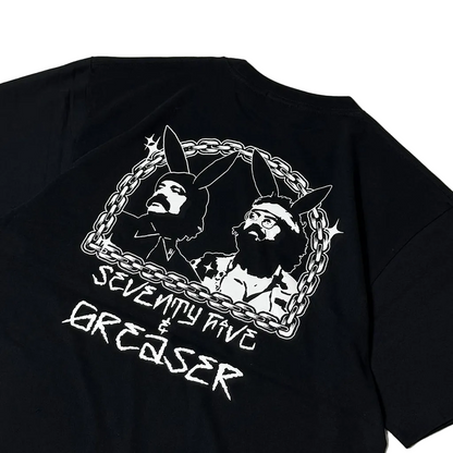 A close-up of a black short-sleeve T-shirt showing the back graphic. The design features a white chain-link border enclosing stylized portraits of two bearded men with bunny ears, with the text 'SEVENTY NINE & GREASER' printed below in a distressed white font.