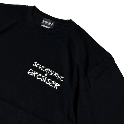 A close-up of a black long-sleeve t-shirt with 'SEVENTY FIVE & GREASER' printed in white stylized text on the chest. The brand label 'GREASER' is visible inside the collar, and the photo is shot on a clean white background.