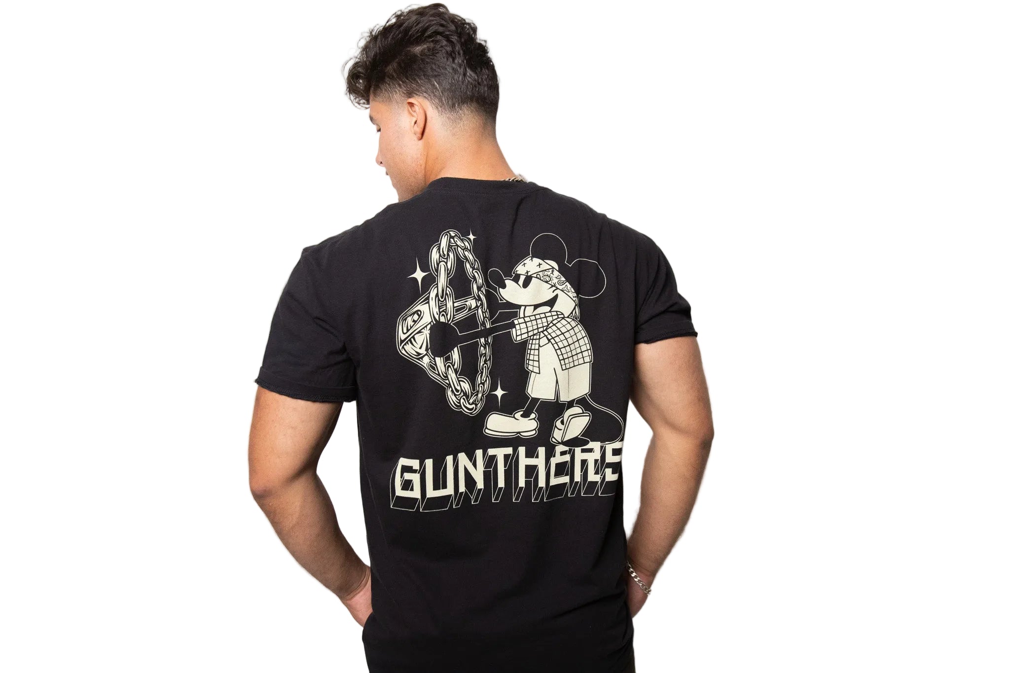 A man viewed from behind wearing a black t-shirt with a large white graphic print on the back. The graphic features a cartoon character and the text 'GUNTHERS