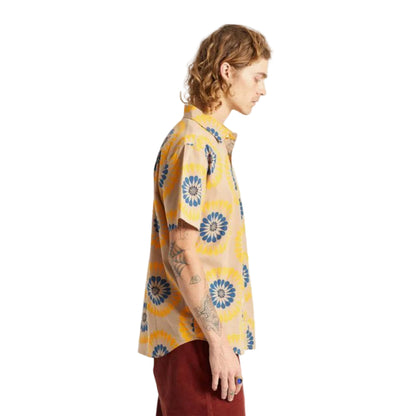 A man shown from the side profile wearing a short-sleeve button-up shirt with a yellow and blue circular floral pattern, paired with dark red pants, against a plain white background.