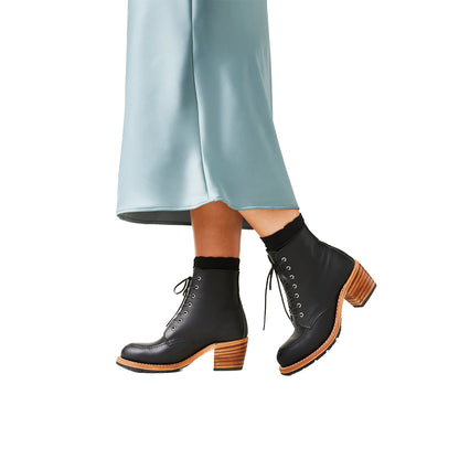 Black ankle boots with brown soles worn with light blue pants on a white background