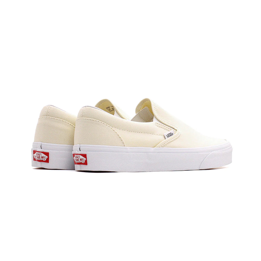 Pair of cream-colored slip-on sneakers with red label on a white background