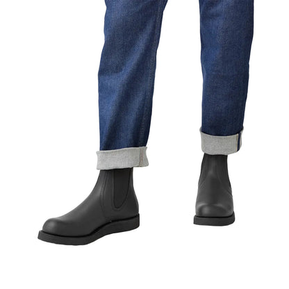 Person wearing black rain boots and blue jeans on a white background