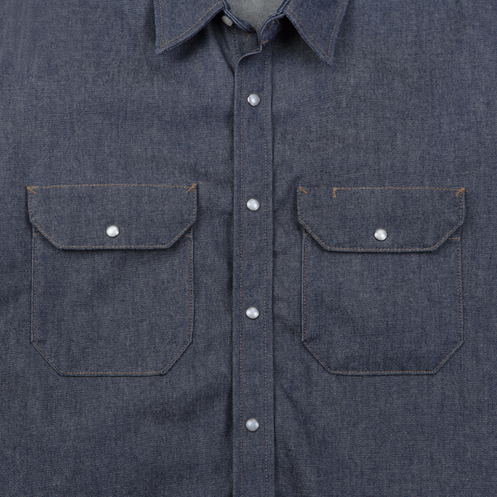 Close-up of a blue denim shirt with two front pockets and button details.