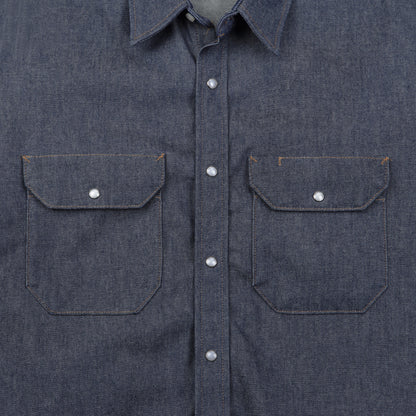 Close-up of a blue denim shirt with two front pockets and button details.