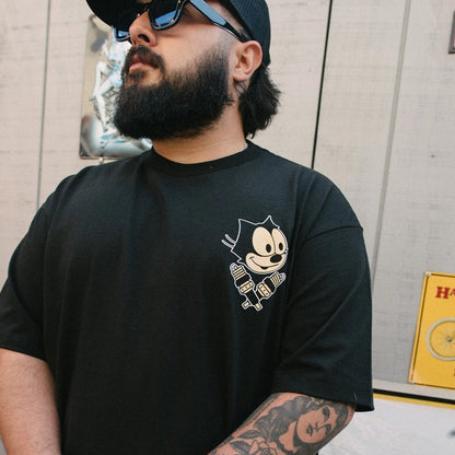 Man wearing a black t-shirt with a graphic design, standing against a light-colored wall.