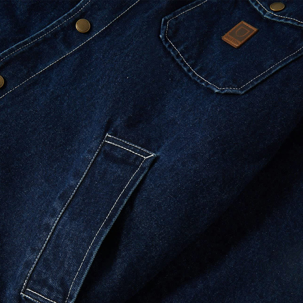 Close-up of a blue denim jacket with a brand logo on the chest pocket.