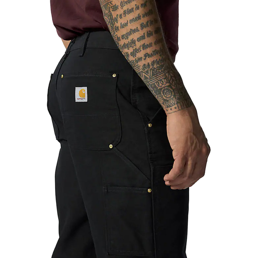 Person wearing black Carhartt work pants with a visible brand logo on a white background