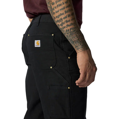 Person wearing black Carhartt work pants with a visible brand logo on a white background