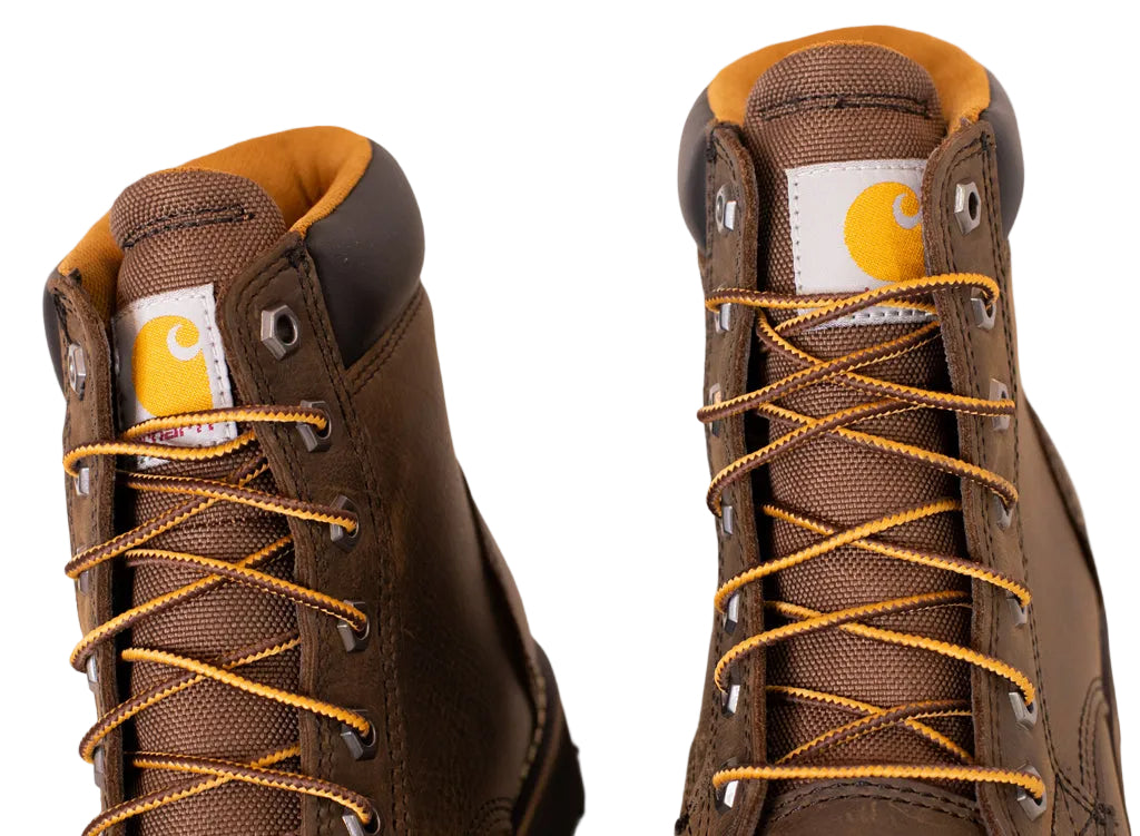 Brown Carhartt boots with yellow laces on a light background