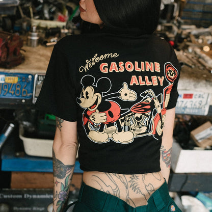 Person wearing a black t-shirt with a graphic design featuring Mickey Mouse and text 'Welcome to Gasoline Alley' in a workshop setting.