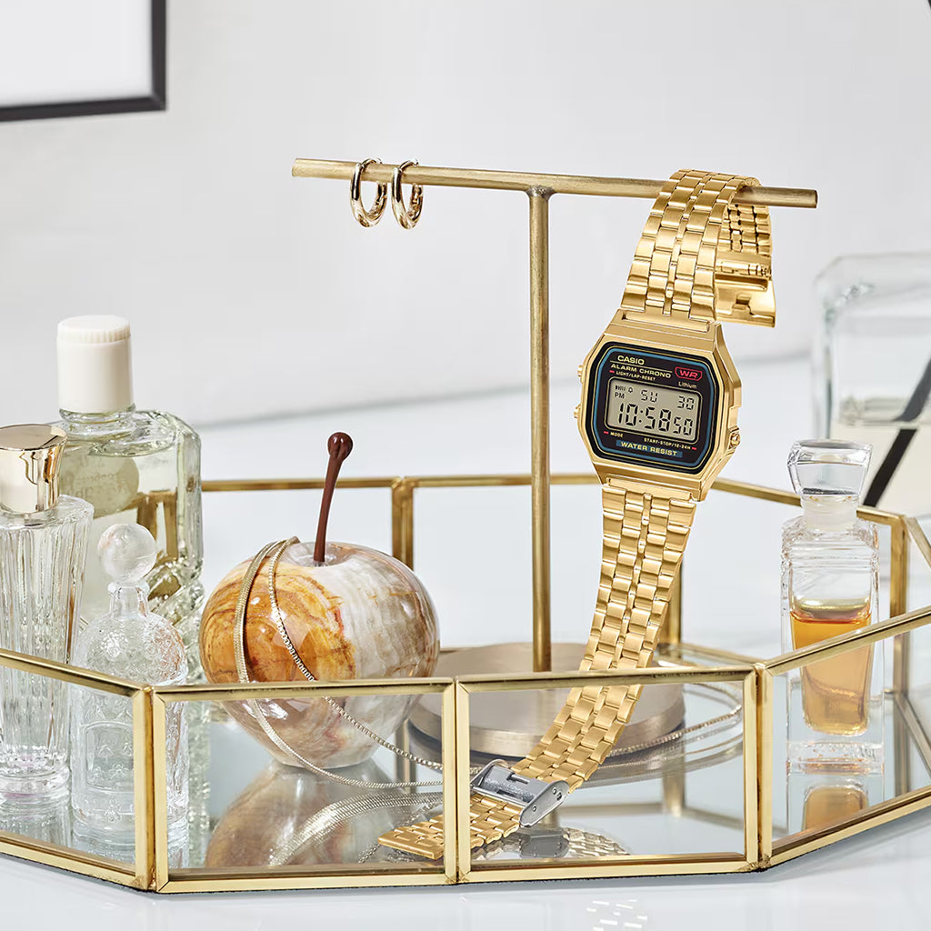 Gold digital watch on a decorative glass stand with other items.
