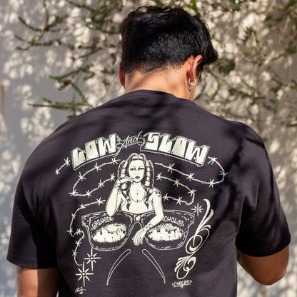 Person wearing a black t-shirt with graphic design and text on the back, standing against a light-colored wall.