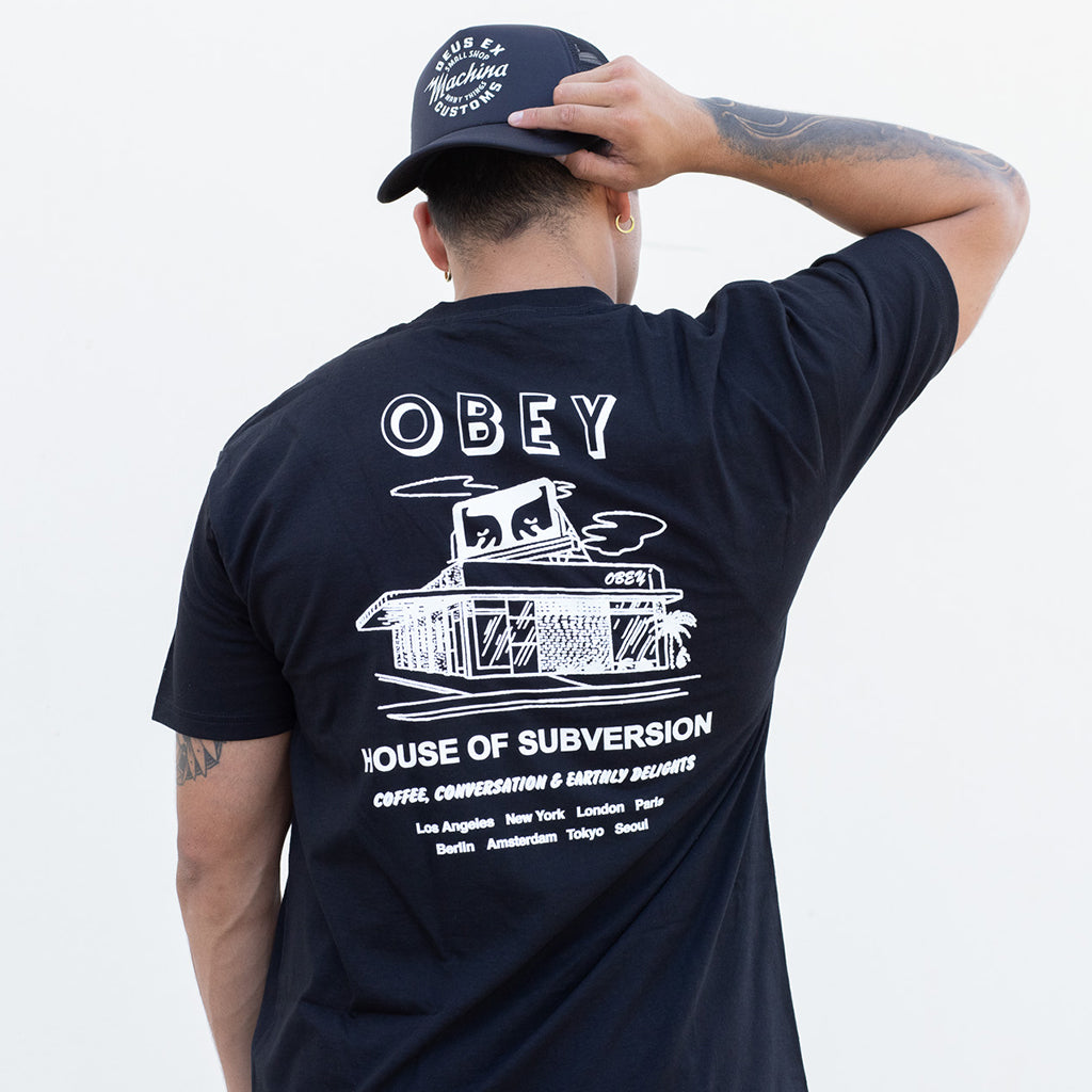 Person wearing a black t-shirt with 'Obey' and 'House of Subversion' design, and a cap.