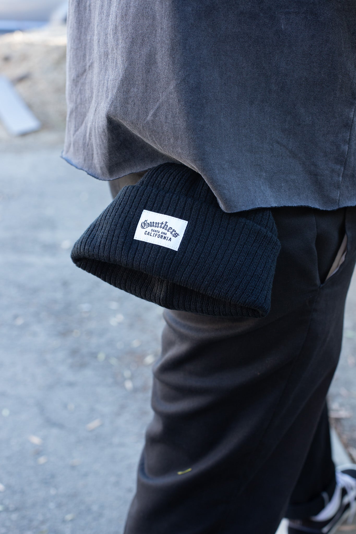 Person wearing a dark blue knit beanie with a logo, standing on a street.