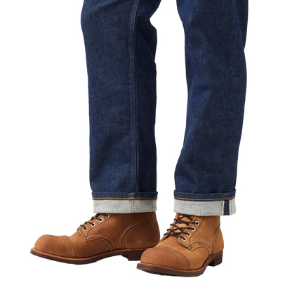 Brown leather boots worn with blue jeans on a light gray background