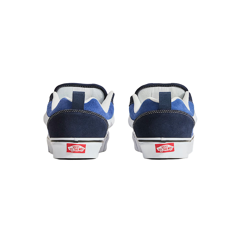 Pair of blue and white sneakers with red Vans logo on a light gray background