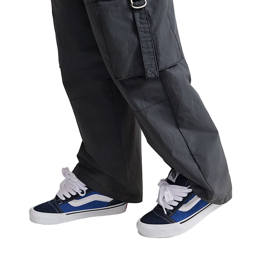 Person wearing dark gray cargo pants and blue sneakers on a light background