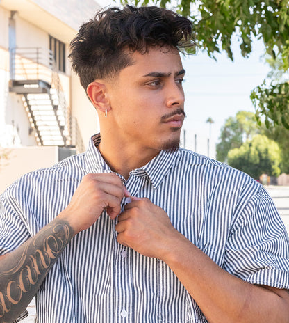 Man adjusting his striped shirt outdoors with a building and trees in the background