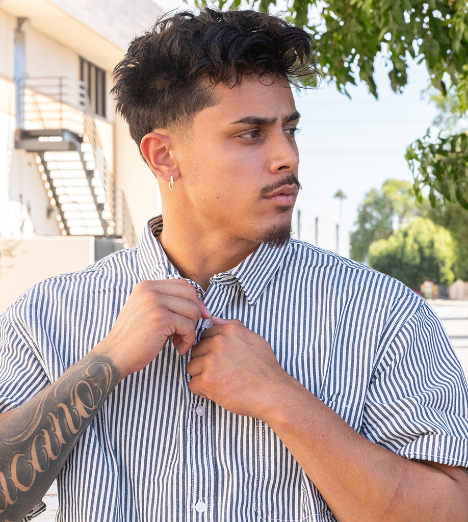 Man adjusting his striped shirt outdoors with a building and trees in the background