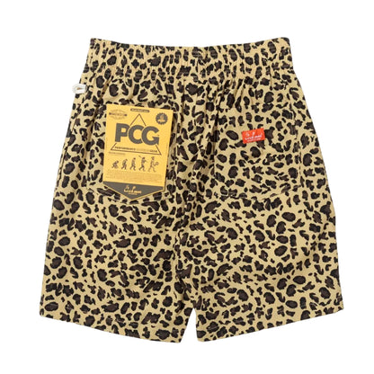 Leopard print shorts in beige and black, featuring a large gold PCG hangtag on the left pocket and a small red Cookman logo tab on the right pocket.