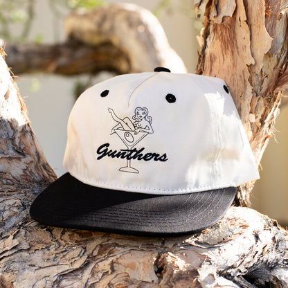 Cap with embroidered design of a woman in a martini glass and 'Gunthers' text sitting on a tree.