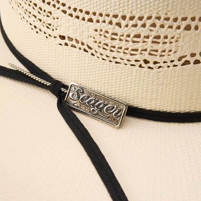 Close-up of a straw hat with a black band and decorative label on a beige background