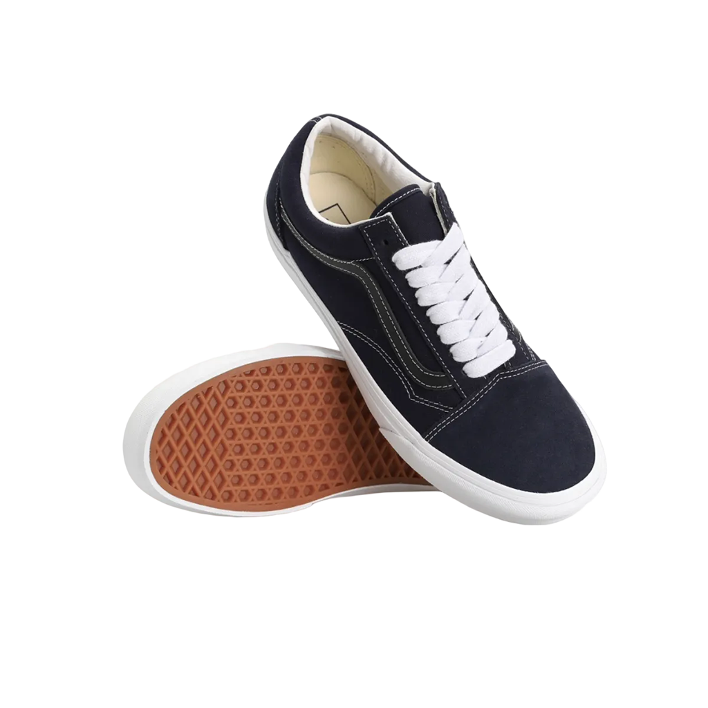 A pair of low-top canvas sneakers in navy blue with white laces and white rubber soles, with one shoe standing upright and the other lying on its side to show the brown textured outsole.