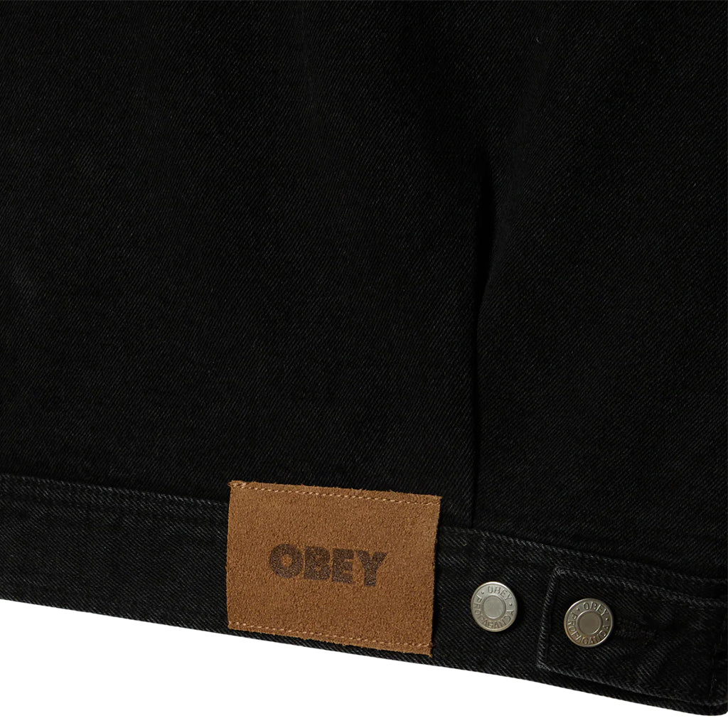 Close-up of a black jacket with a brown leather patch displaying 'OBEY' on a white background.