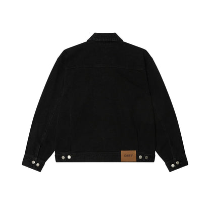 Back of faded black denim trucker jacket with brown obey patch on bottom of jacket. Laying flat on a white background